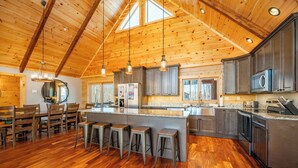 A spacious kitchen with wooden beams, a large island with stools, and modern appliances. - Spacious Mountain Lodge w/ Hot Tub & Fire Pit (McHenry)