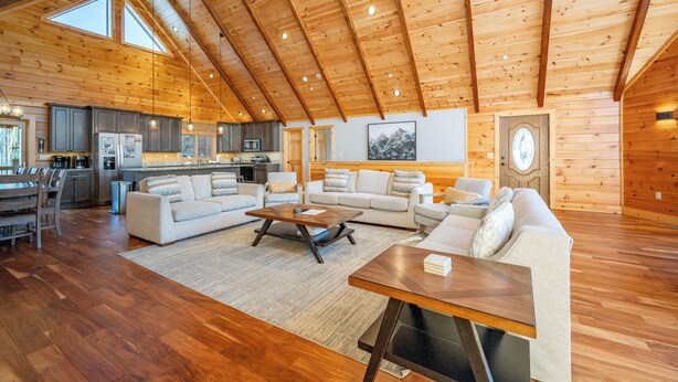 A spacious living area with a high ceiling and wooden beams, a kitchen with modern appliances, and a cozy seating arrangement. - Spacious Mountain Lodge w/ Hot Tub & Fire Pit (McHenry)
