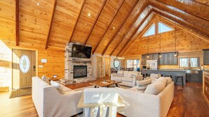 A spacious living area with a fireplace, wooden ceiling, and a kitchen area with a large island. - Spacious Mountain Lodge w/ Hot Tub & Fire Pit (McHenry)