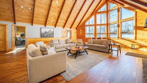 A spacious living room with wooden beams, large windows, and a cozy fireplace. - Spacious Mountain Lodge w/ Hot Tub & Fire Pit (McHenry)