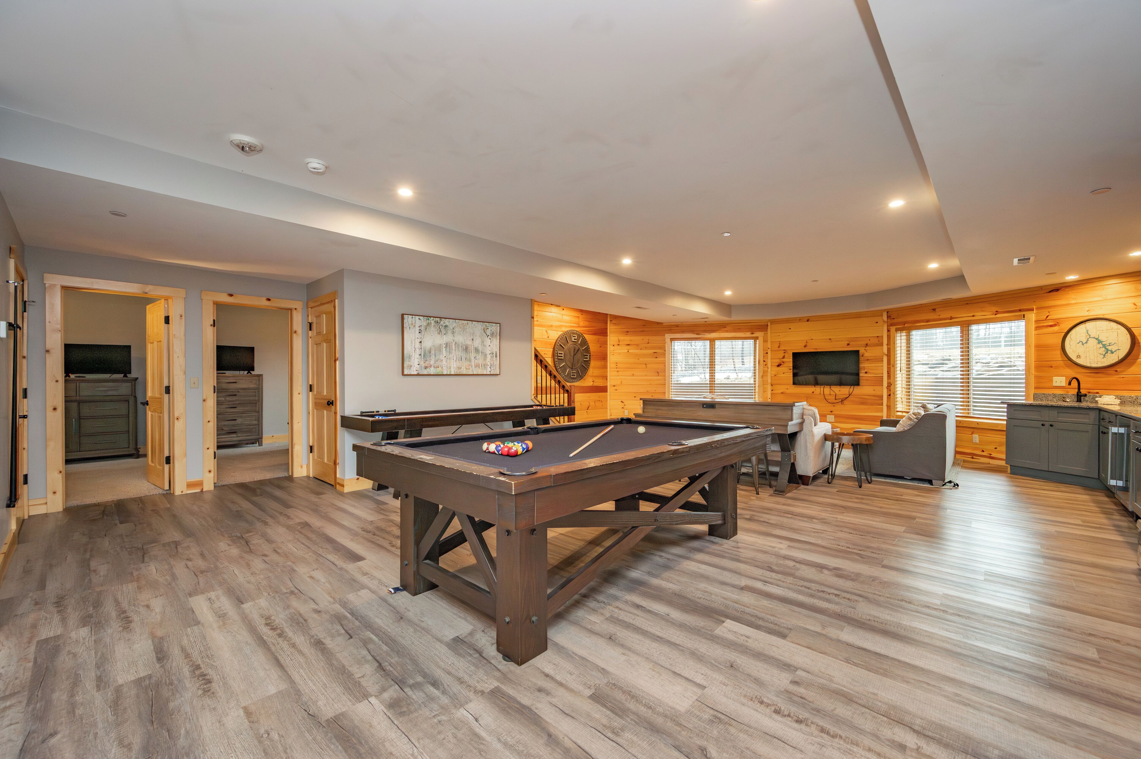 Una habitación amplia con mesa de billar, piso de madera y zona de cocina.