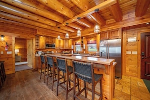 A wooden cabin interior with a kitchen, bar stools, and a refrigerator.