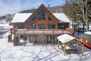 A log cabin with a balcony, wooden deck, and a snow-covered roof.