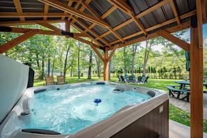 A hot tub under a wooden pergola with a view of a grassy area and trees. - Stylish Lakefront Escape w/ Hot Tub, Bar & Dock (Oakland)