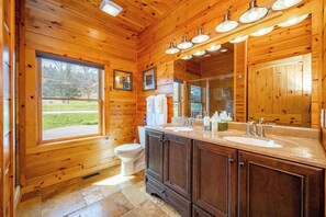 Bagno di una baita in legno con un'ampia finestra, un WC, un lavandino con specchio e mobili in legno.