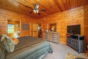 Camera da letto in una baita di legno, con un letto, una cassettiera, un televisore e una ventola a soffitto.