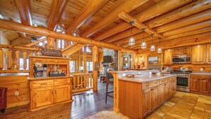 A spacious kitchen with wooden cabinets, a large island, and a stone fireplace. - Stylish Lakefront Escape w/ Hot Tub, Bar & Dock (Oakland)
