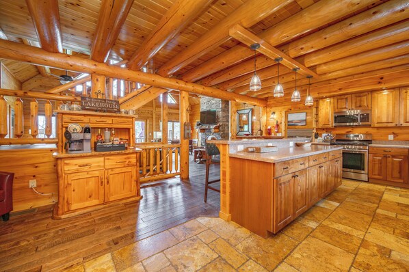 A spacious kitchen with wooden cabinets, a large island, and a stone fireplace. - Stylish Lakefront Escape w/ Hot Tub, Bar & Dock (Oakland)
