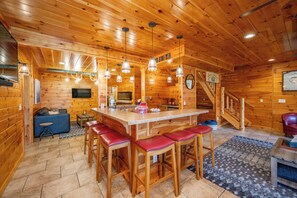 A wooden interior with a bar area, stools, a sofa, and a staircase.