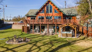 A log cabin with a large deck, outdoor seating, and a hot tub. - Stylish Lakefront Escape w/ Hot Tub, Bar & Dock (Oakland)