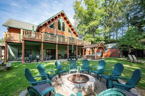 A log cabin with a covered porch, outdoor seating, and a fire pit. - Stylish Lakefront Escape w/ Hot Tub, Bar & Dock (Oakland)