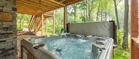 A hot tub with a wooden deck and stone wall, surrounded by a forest.