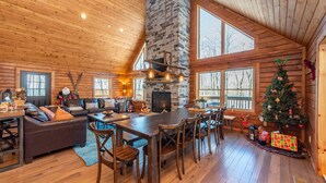 A cozy cabin interior with a stone fireplace, wooden dining table, and a Christmas tree. - Woodsy Retreat Near Wisp w/ Golf & Hot Tub (McHenry)