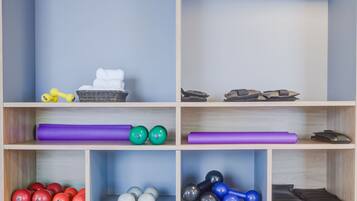 A storage unit with multiple shelves, some containing exercise equipment like dumbbells and yoga mats, and others holding items like towels and a basket.