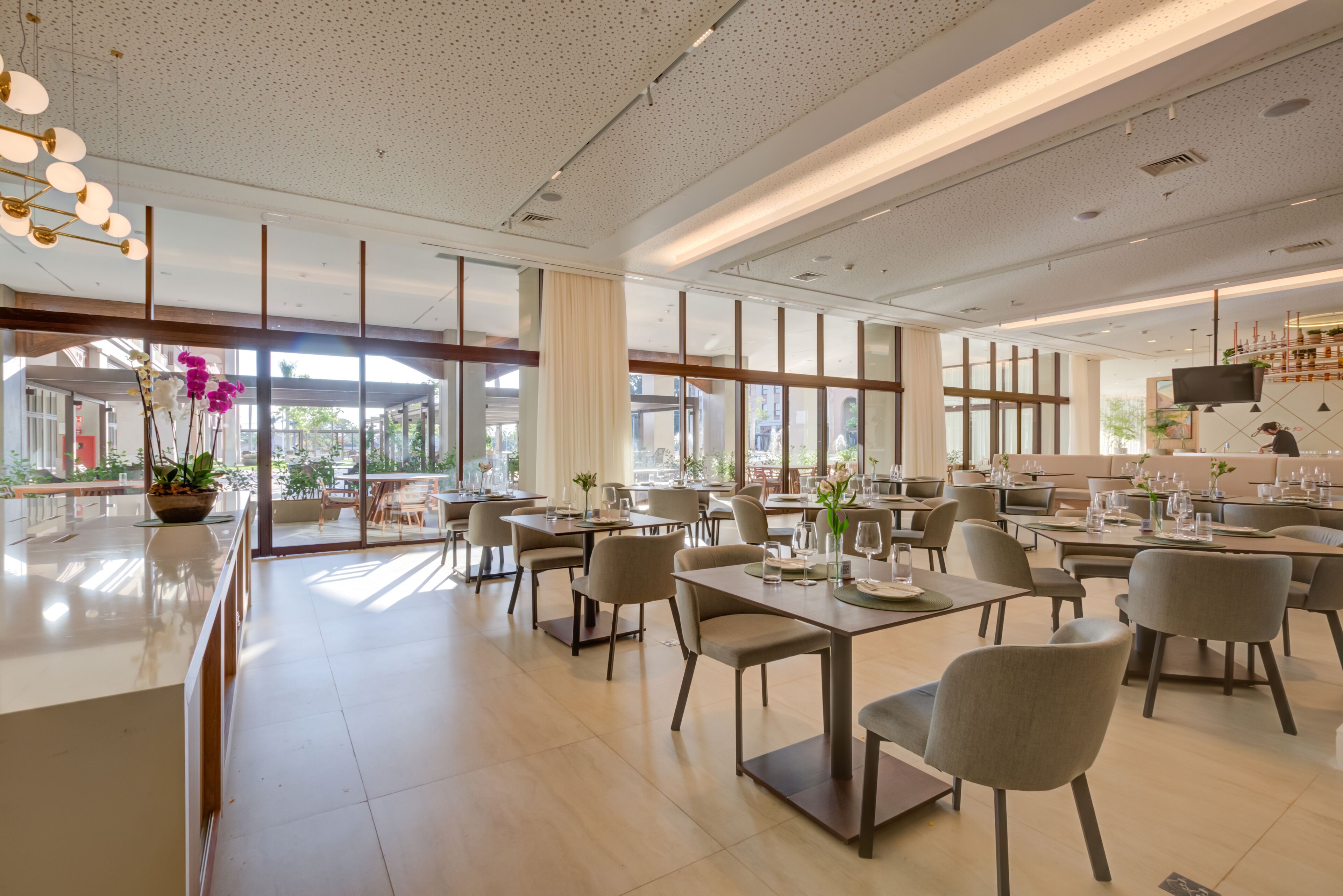 A spacious restaurant with high ceilings, large windows, and modern furnishings.