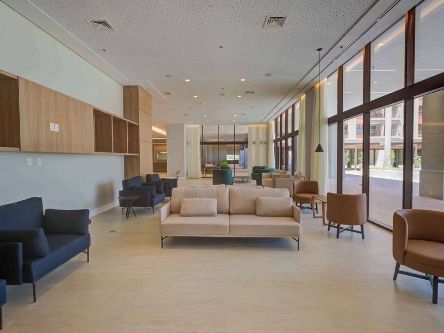 A spacious lobby with a beige sofa, blue and brown chairs, wooden paneling, and large windows offering views of the outside.