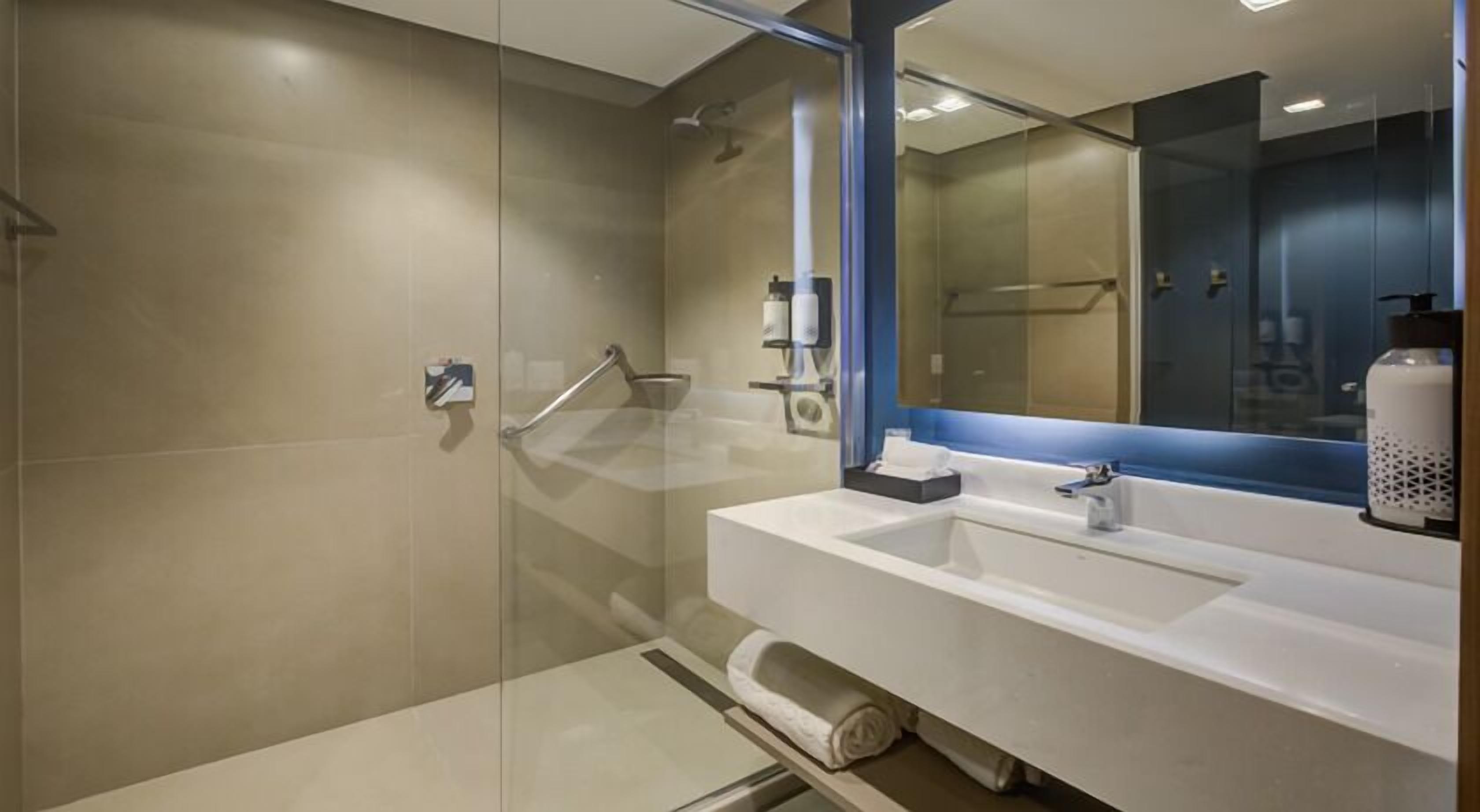 A modern bathroom with a glass shower enclosure, a white sink with a mirror, and a towel rack.