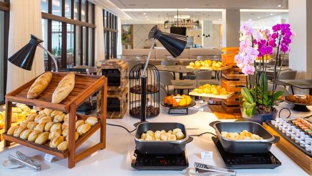 Uma mesa de buffet com diversos alimentos, incluindo pão, doces e uma seleção de frutas e vegetais.