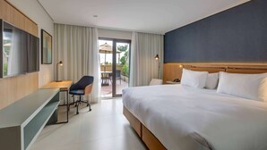 Quarto de hotel com uma cama grande, uma escrivaninha, uma cadeira e uma televisão.