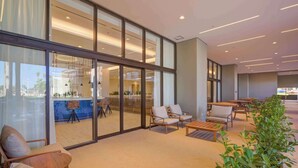 Um hall de hotel moderno com paredes de vidro, áreas de estar e uma piscina visível.