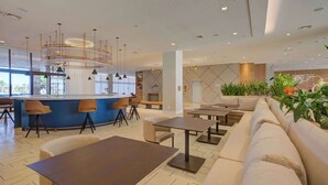 Um lobby moderno de hotel com área de bar, assentos e uma grande planta.