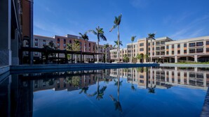 Um hotel com piscina espelhada, palmeiras e arquitetura moderna.