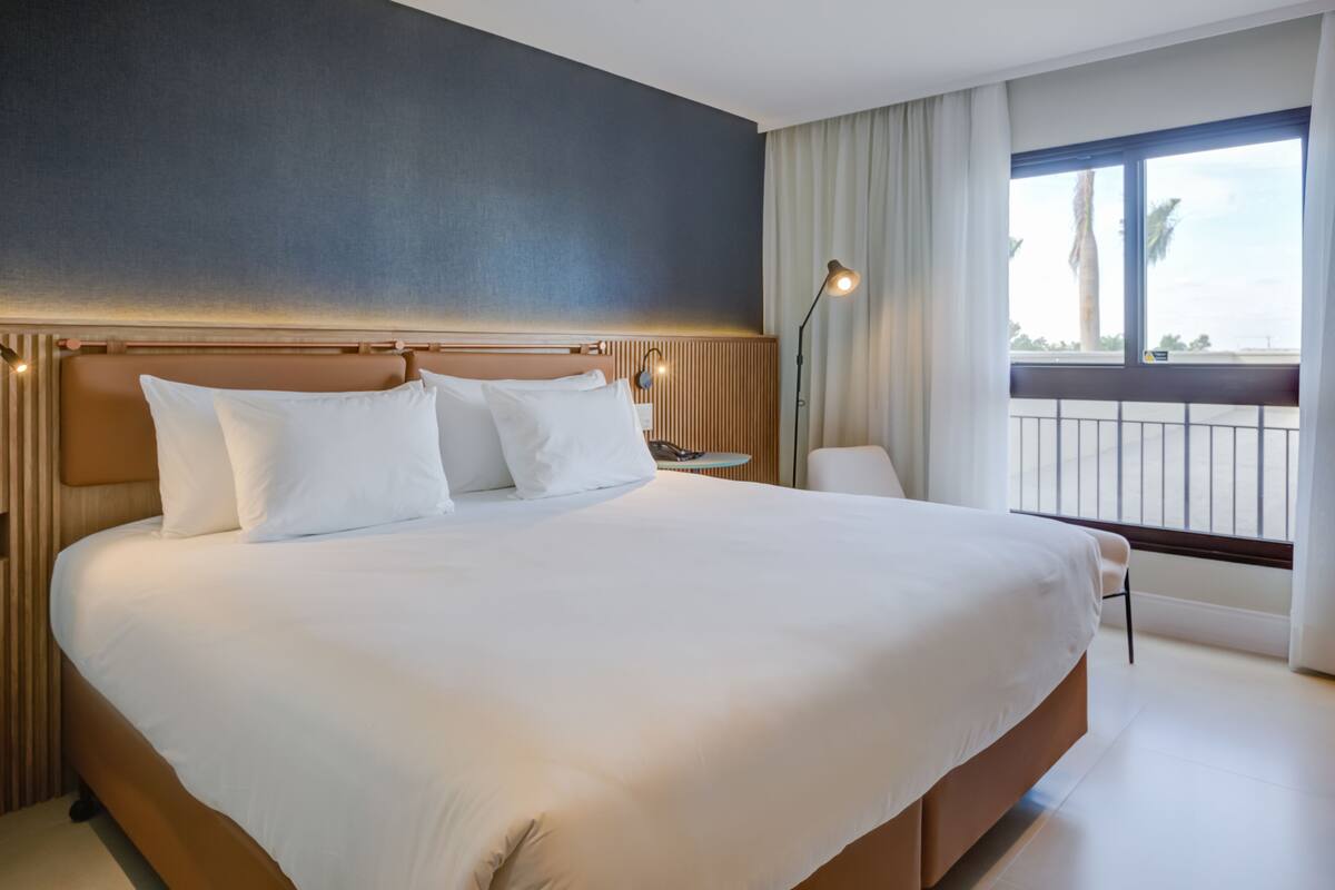 A large bed with white linens, a wooden headboard, and a nightstand with a lamp.