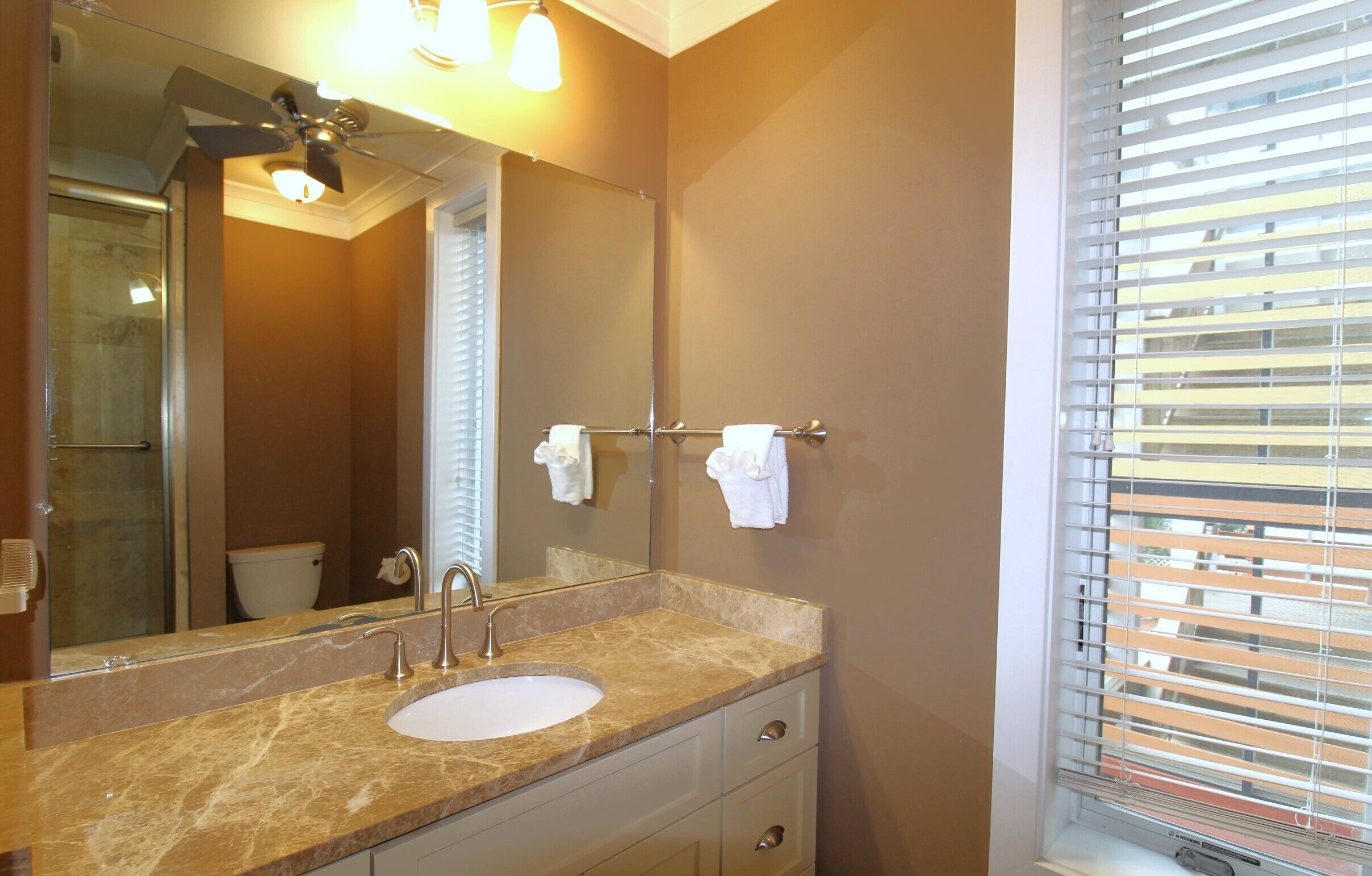 A bathroom with a marble countertop, a sink, a mirror, and a towel rack.
