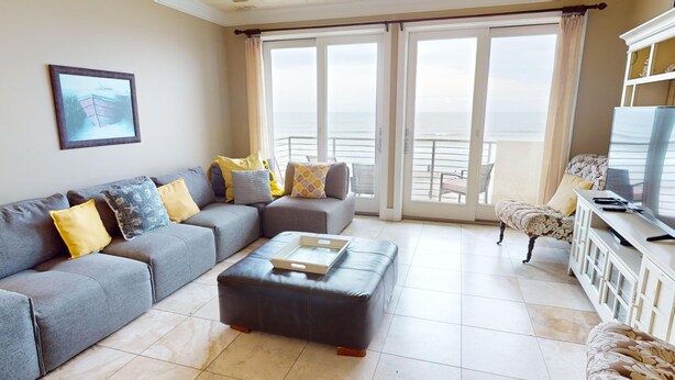 A living room with a grey sofa, ottoman, and a television on a stand. - Lavish Oceanfront Townhome- Whispering Palms (Folly Beach)