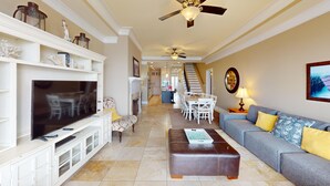 A spacious living room with a flat-screen TV, a sofa, a coffee table, and a staircase leading to the upper floor. - Lavish Oceanfront Townhome- Whispering Palms (Folly Beach)