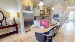 A modern kitchen with a central island, stainless steel appliances, and a dining area with bar stools. - Lavish Oceanfront Townhome- Whispering Palms (Folly Beach)