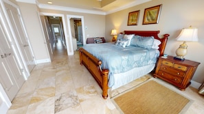 A bedroom with a bed, nightstands, a dresser, a rug, and a hallway leading to another room.