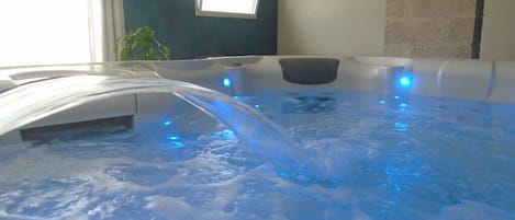 Un jacuzzi con iluminación azul, una ventana y una planta al fondo.