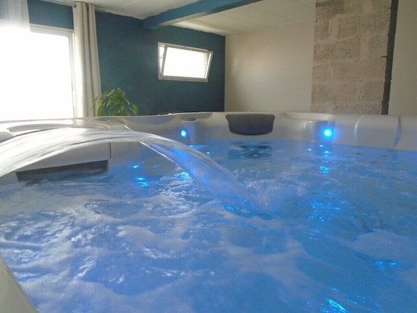 A hot tub with blue lighting, a window, and a plant in the background.