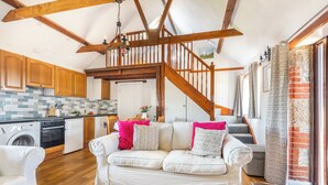 A cozy living room with a sofa, a staircase, wooden beams, and a kitchen area. - 2 Bed cottage, log burner. Pet friendly - 5 mins to nearest beach. (Port Isaac)