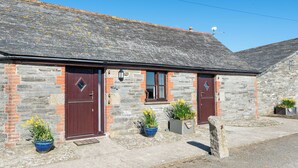 A stone cottage with two red doors, a small window, and potted plants in front. - 2 Bed cottage, log burner. Pet friendly - 5 mins to nearest beach. (Port Isaac)