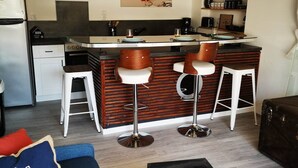 A compact kitchen with a central island, bar stools, a dining table, and a sofa with a cushion. - Ultra cosy small house (Piriac-sur-Mer)