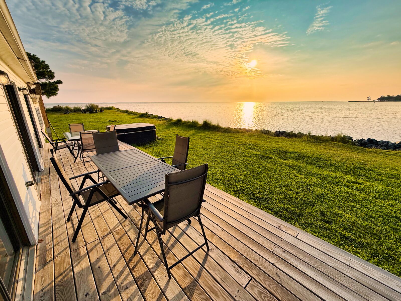 A deck with a table and chairs overlooking a body of water at sunset.