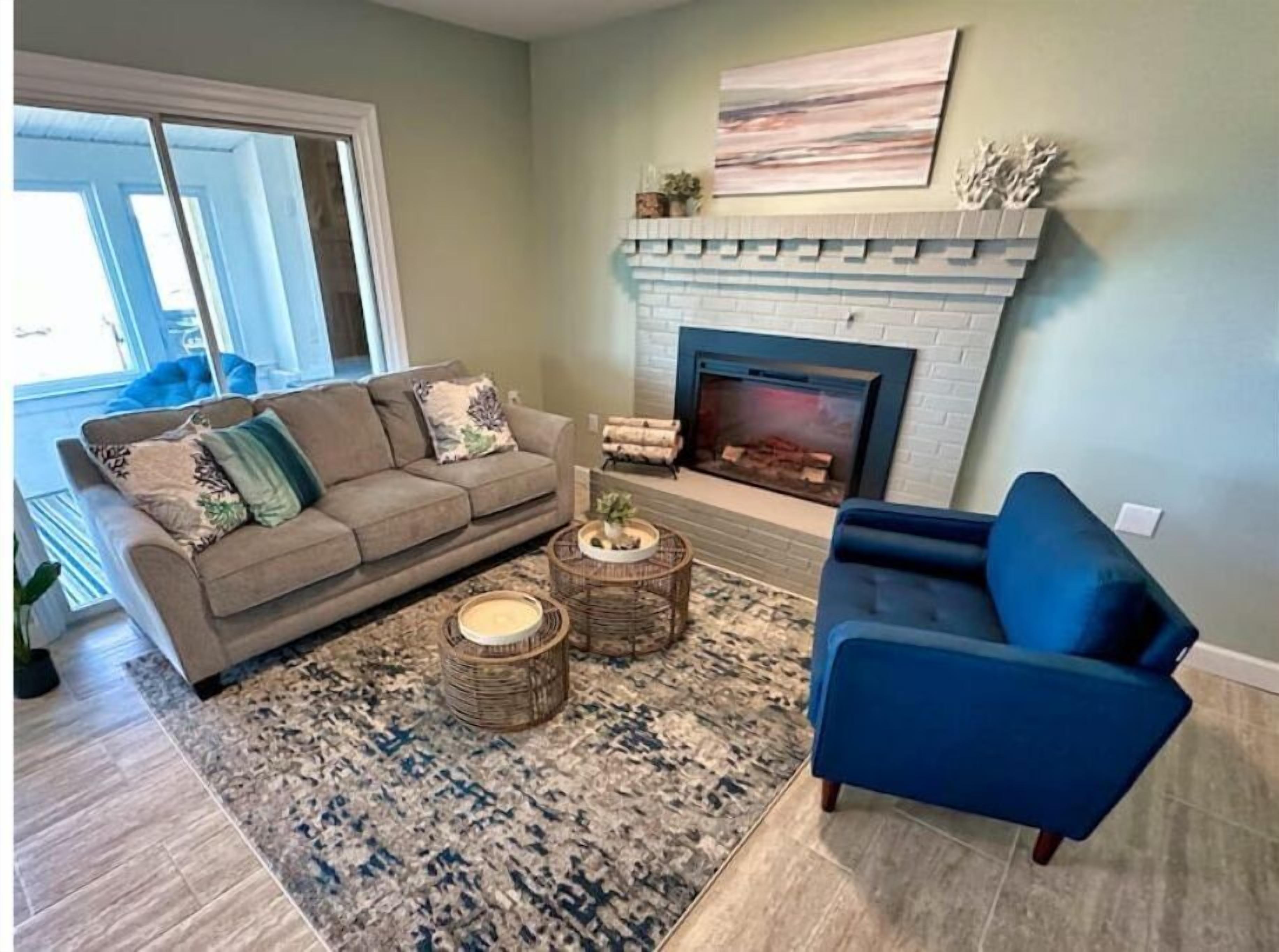 Un salon avec une cheminée, un canapé, un fauteuil bleu et un tapis à motifs.