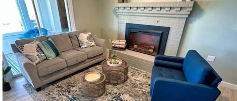 Un salon avec une cheminée, un canapé, un fauteuil bleu et un tapis à motifs.