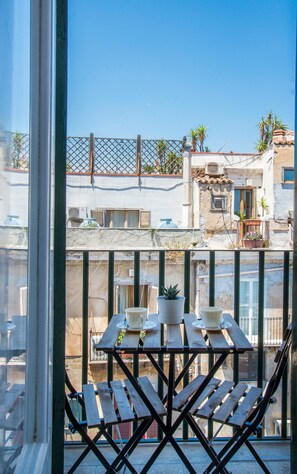 A balcony with a table and chairs, overlooking a residential area with buildings and palm trees.
