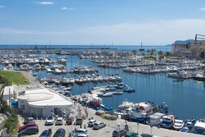 A marina with numerous boats docked, a parking area with cars, and a building with a sign.