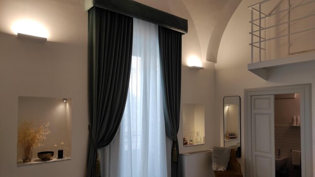 Una habitación de hotel moderna con una cama grande, un área de descanso con una silla, una tocador con espejo y un baño visible a través de una puerta abierta.