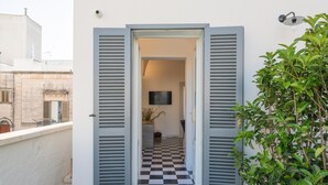 Una entrada moderna con contraventanas grises, suelo a cuadros y una planta en maceta a la derecha.