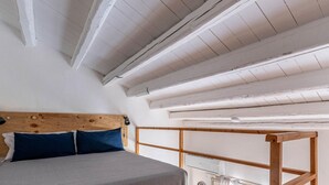 A bedroom with a wooden headboard, a bed with grey bedding, and a white ceiling with exposed beams. - Sant Onofrio Mini Loft by Wonderful Italy (Palermo)