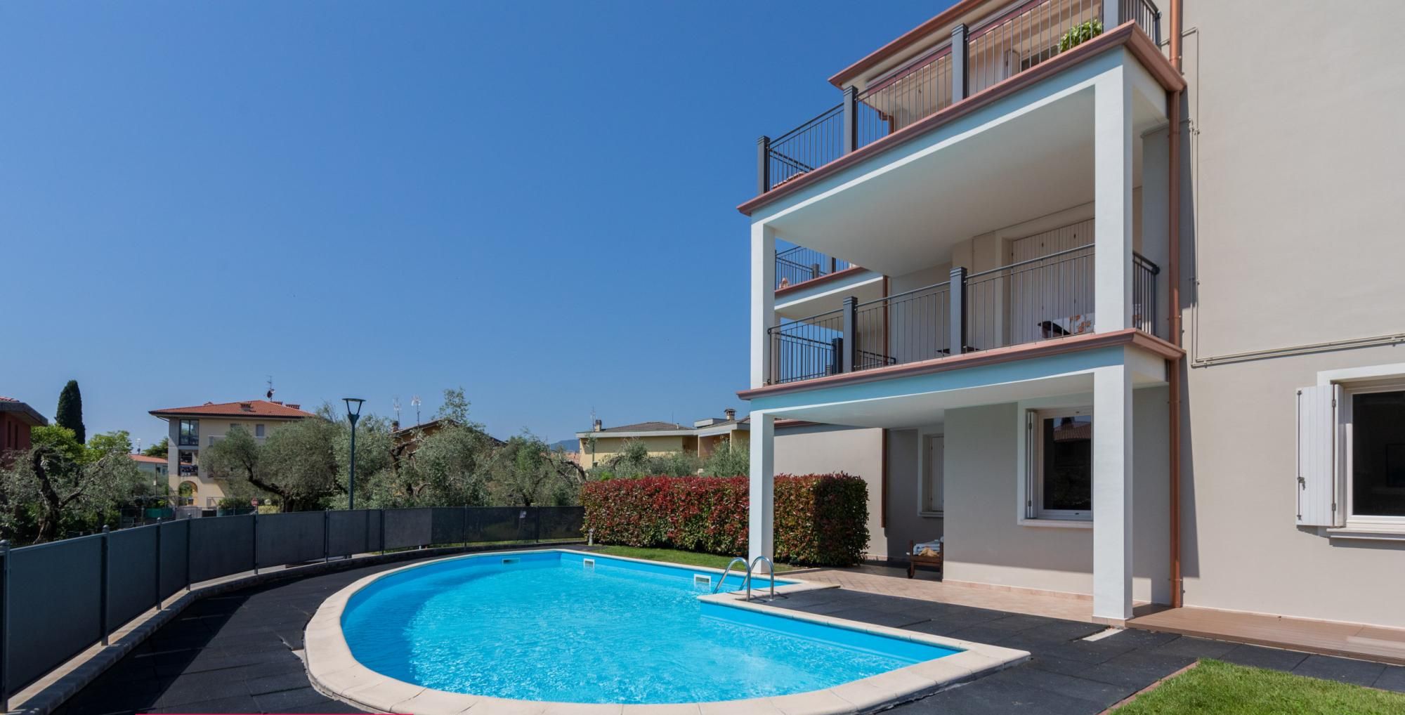 A modern two-story house with a swimming pool, a balcony, and a well-maintained lawn.