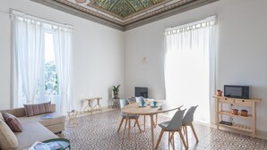 A spacious living room with a round wooden table, two sofas, a TV, and a ceiling with intricate patterns. - Casa Darsena With Sea View Balcony by Wonderful Italy (Syracuse)