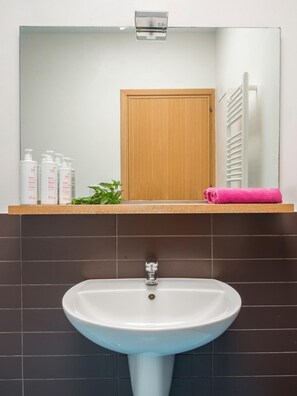 Kylpyhuoneessa on valkoinen pesuallas, sen yläpuolella peili ja taustalla puinen ovi.