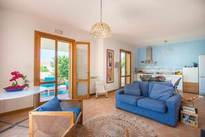 A modern living room with a blue sofa, a dining area with a table and chairs, a kitchen with a blue backsplash, and a large window. - Calarossa Seaview by Wonderful Italy (Terrasini)