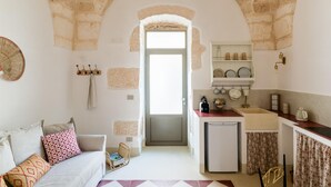 A cozy room with a stone archway leading to a kitchen area, a small refrigerator, and a dining table with chairs.